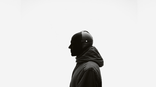 Mann in komplett schwarz mit einer Maske steht vor einem weißen Hintergrund 