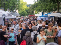 Eine dichte Menschenmenge schlendert zwischen Marktständen mit Essen, Kunsthandwerk und Streetfood entlang.