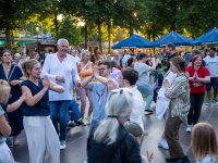 Menschen mit und ohne Behinderung tanzen gemeinsam auf einer Freifläche unter Bäumen bei sommerlichem Abendlicht.