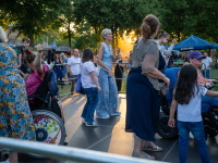 Menschen in Rollstühlen und Fußgängerinnen bewegen sich gemeinsam auf einer Bühne bei goldener Abendstimmung.