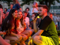 Ein Musiker sitzt mitten im Publikum, hält ein Mikrofon und unterhält sich lächelnd mit jungen Fans.
