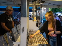 Eine junge Frau begutachtet Schmuck an einem Marktstand beim Altstadtfest. Der Verkäufer steht dahinter und beobachtet sie. I