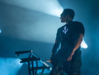 Der Keyboarder von „Two Colors“ steht vor seinem Instrument im blauen Bühnenlicht. Er trägt Sonnenbrille und ein Shirt mit beleuchtetem Ankersymbol, im Hintergrund dramatische Lichtprojektionen.