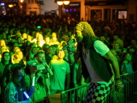 Mitglieder von „Oku & the Reggaerockers“ spielen energiegeladen auf der Bühne. Links der Sänger mit Dreadlocks und erhobenem Arm, rechts eine Saxophonistin in weißem Sommerkleid. Die Bühne ist in grünes Licht getaucht.