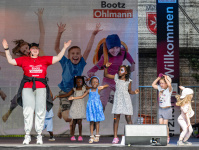 Tanzlehrerin und Kinder auf einer Bühne bei einer Tanzvorführung, im Hintergrund fröhliche Banner.