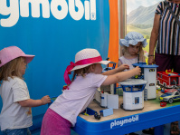 Mehrere Kinder spielen an einem Spieltisch mit Playmobil-Gebäuden.