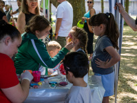 Mädchen bekommt an einem Schminkstand auf einem Fest Gesichtsbemalung, weitere Kinder warten daneben.