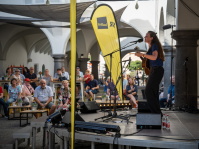 Sängerin mit Gitarre steht auf einer kleinen Bühne, Publikum sitzt an Tischen und schaut zu.