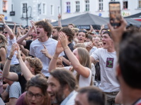 Die Menge feiert begeistert vor der Bühne, junge Menschen jubeln, klatschen und rufen ausgelassen, einige springen vor Freude.