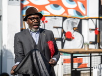 Ein eleganter Mann in Anzug und Trilby-Hut führt herzlich lachend Kunststücke vor