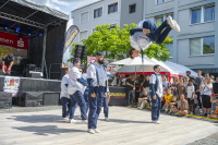 Breakdancer macht spektakulären Flip über Regenschirm, Tänzer-Crew und Publikum schauen zu.