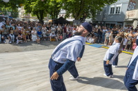 Tänzer in Hemd und Hosenträgern performt vor großer Menschenmenge auf einem Platz.