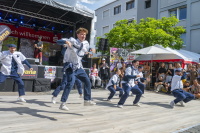 Tanzgruppe in einheitlichen Hemden und Krawatten performt energiegeladene Choreo vor Bühne.
