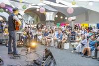 Sänger mit Akustikgitarre spielt vor sitzendem Publikum unter bunten Lampions.