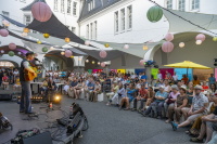 Gitarrist singt für sitzendes Publikum im lampiongeschmückten Innenhof am Abend.