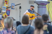 Straßenmusiker mit Schiebermütze singt lächelnd zur Akustikgitarre vor Publikum.