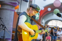 Gitarrist mit Schiebermütze konzentriert beim Musik machen, Lampions im Hintergrund.