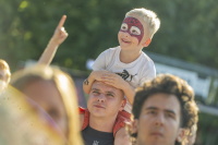 Lachender Junge mit Spiderman-Schminke sitzt auf den Schultern eines Mannes.