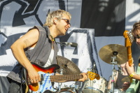 Lachender Bassist mit Sonnenbrille rockt begeistert auf der Bühne vor Schlagzeug.