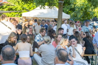Menschen sitzen und stehen entspannt an Bierbänken unter Bäumen beim Festbetrieb.