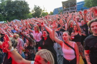 Riesige Menschenmenge tanzt mit erhobenen Armen im roten Bühnenlicht bei Konzert.