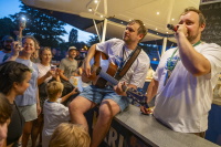 Sänger und Gitarrist auf Bartresen performen abends dicht umringt von Publikum.