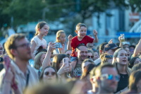 Lachender Junge im roten Shirt sitzt jubelnd auf den Schultern seines Vaters.