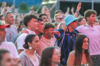 Junge Männer mit Arm um die Schulter singen ausgelassen mit bei Konzert.