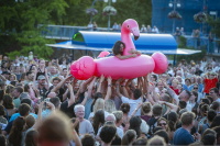 Aufblasbarer pinker Flamingo mit Frau darauf wird von jubelnder Menge getragen.