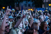 Begeisterte Konzertmenge bei Nacht, eine Frau formt mit den Händen ein Herz über dem Kopf, viele Arme erhoben.