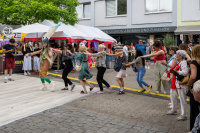 Sambatänzerin im Federkostüm führt Besucherkette an, Menschen fassen sich an den Schultern beim Straßenfest.