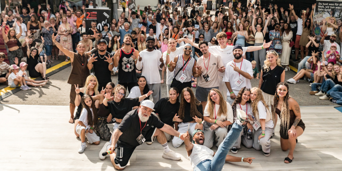 Großes Gruppenfoto mit jubelndem Publikum im Hintergrund